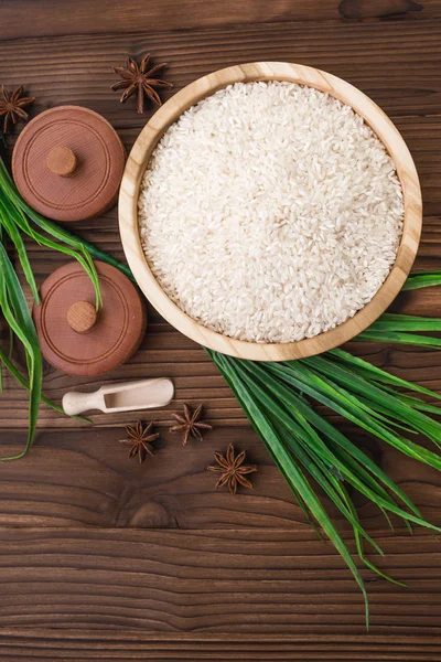 Riso in piatto di legno e anice su fondo di legno marrone. Riso e spezie in contenitore ecologico. Pronti per la cottura. Set per spa . — Foto Stock