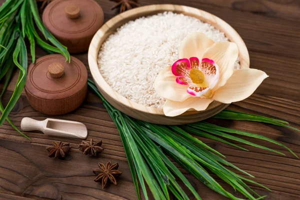 Arroz en plato de madera y anís sobre fondo de madera marrón. Arroz y especias en contenedor ecológico. Listos para cocinar. Set para spa . — Foto de Stock