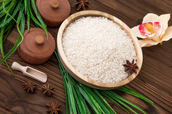 Arroz en plato de madera y anís sobre fondo de madera marrón. Arroz y especias en contenedor ecológico. Listos para cocinar. Set para spa . — Foto de Stock