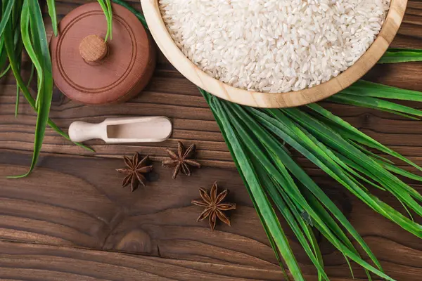 Arroz en plato de madera y anís sobre fondo de madera marrón. Arroz y especias en contenedor ecológico. Listos para cocinar. Set para spa . — Foto de Stock