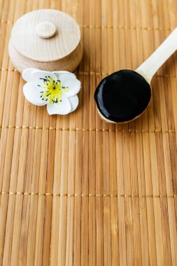 Bambu bir arka plan üzerine bir tahta kaşık içinde siyah bir madde. Siyah maske