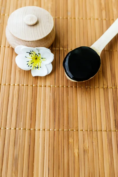 Bambu bir arka plan üzerine bir tahta kaşık içinde siyah bir madde. Siyah maske