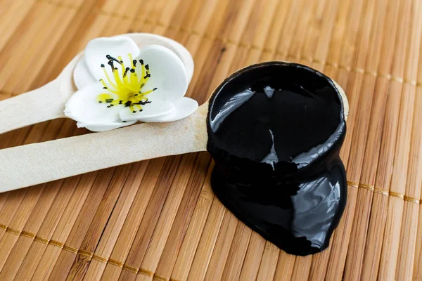 Bambu bir arka plan üzerine bir tahta kaşık içinde siyah bir madde. Siyah maske — Stok fotoğraf
