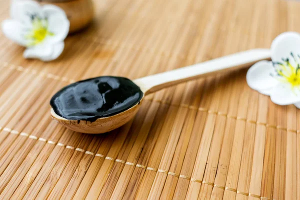 Bambu bir arka plan üzerine bir tahta kaşık içinde siyah bir madde. Siyah maske