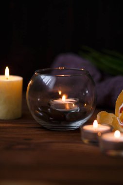 Bir mum bir cam vazo, dekorasyon ve koyu ahşap arka plan üzerinde çeşitli ilginç unsurlar. Yanan mumlar. Spa için ayarla ve masaj.