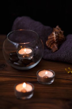 Bir mum bir cam vazo, dekorasyon ve koyu ahşap arka plan üzerinde çeşitli ilginç unsurlar. Yanan mumlar. Spa için ayarla ve masaj.