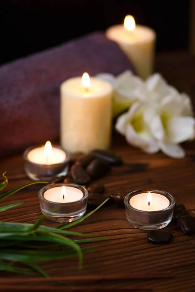 Uma vela em um vaso de vidro, decoração e vários elementos interessantes em um fundo de madeira escuro. Velas a arder. Conjunto para spa e massagem . — Fotografia de Stock