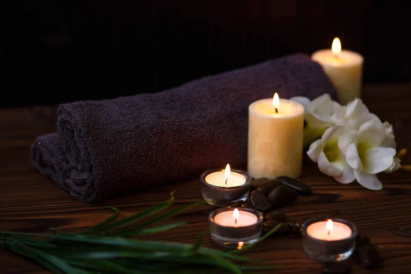 Una vela en un jarrón de vidrio, decoración y varios elementos interesantes sobre un fondo de madera oscura. Velas encendidas. Set para spa y masaje . — Foto de Stock