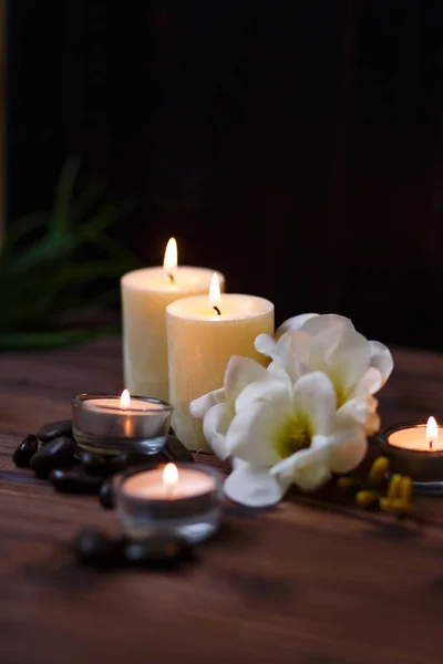 Uma vela em um vaso de vidro, decoração e vários elementos interessantes em um fundo de madeira escuro. Velas a arder. Conjunto para spa e massagem . — Fotografia de Stock