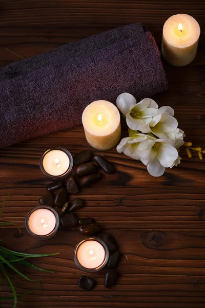 Uma vela em um vaso de vidro, decoração e vários elementos interessantes em um fundo de madeira escuro. Velas a arder. Conjunto para spa e massagem . — Fotografia de Stock