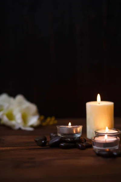 Uma vela em um vaso de vidro, decoração e vários elementos interessantes em um fundo de madeira escuro. Velas a arder. Conjunto para spa e massagem . — Fotografia de Stock