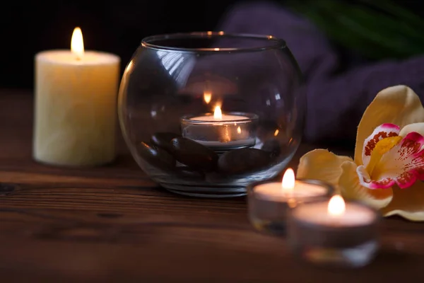 Svíčka ve skleněné váze, dekorace a různé zajímavé prvky na tmavém pozadí dřevěná. Hořící svíčky. Pro wellness a masáže. — Stock fotografie