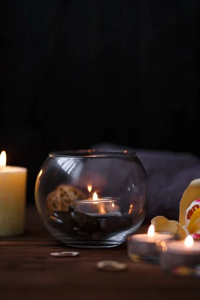 Uma vela em um vaso de vidro, decoração e vários elementos interessantes em um fundo de madeira escuro. Velas a arder. Conjunto para spa e massagem . — Fotografia de Stock