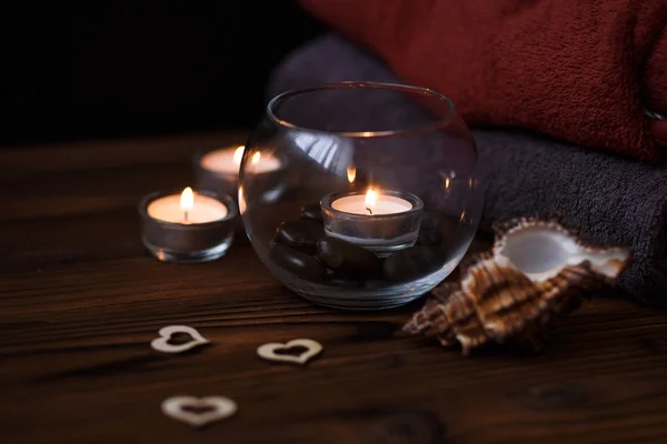 Una vela en un jarrón de vidrio, decoración y varios elementos interesantes sobre un fondo de madera oscura. Velas encendidas. Set para spa y masaje . — Foto de Stock