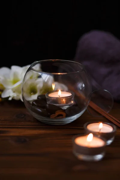 Una vela en un jarrón de vidrio, decoración y varios elementos interesantes sobre un fondo de madera oscura. Velas encendidas. Set para spa y masaje . —  Fotos de Stock