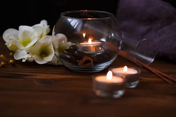 Una vela en un jarrón de vidrio, decoración y varios elementos interesantes sobre un fondo de madera oscura. Velas encendidas. Set para spa y masaje . — Foto de Stock