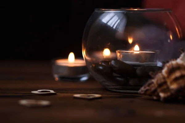 Una vela en un jarrón de vidrio, decoración y varios elementos interesantes sobre un fondo de madera oscura. Velas encendidas. Set para spa y masaje . Imagen De Stock