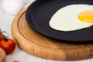 Yumurta kiraz domates, roka, tuz ile siyah bir tavada kızarmış tavuk. Bir beyaz tahta masada Kahvaltı. 