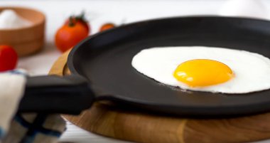 Yumurta kiraz domates, roka, tuz ile siyah bir tavada kızarmış tavuk. Bir beyaz tahta masada Kahvaltı. 