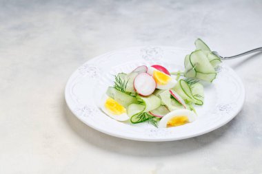 Beyaz tabakta haşlanmış yumurta ile yeşil sebze salatası. Çelik çatalda salatalık. Mermer tezgahın üstünde. görünümü kapat