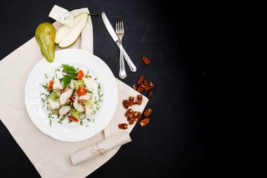Armutlu salata, Gorgonzola ve ceviz. Siyah bir masada, çatal ve bıçağın yanında duran beyaz bir tabakta. Yukarıdan görünüm