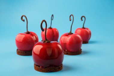 Mavi arka planda kiraz şeklinde parlak kremalı kekler.