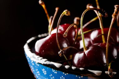 Siyah arka planda mavi bir kasede vişne.