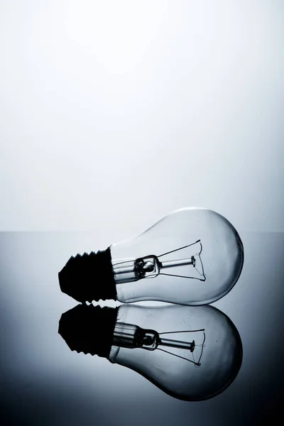 Incandescent lamp lying on a table on a gray gradient background with reflection