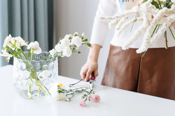 A girl florist makes a bouquet on a white table