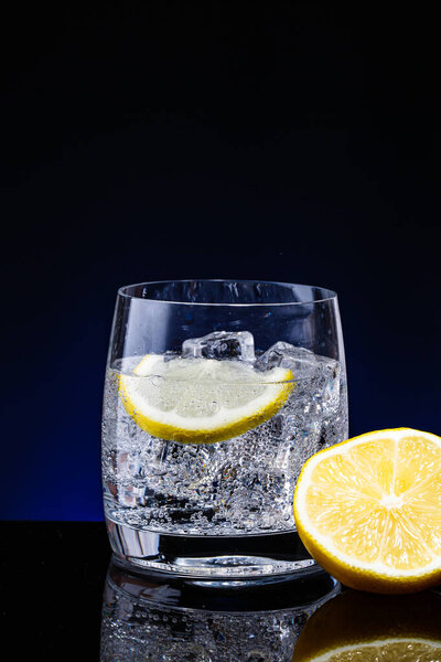 Glass glass of water with lemon on the dark background. Mountain mineral pure mountain water with gas bubbles and a lemon slice and spray tonic refreshing sports drink.