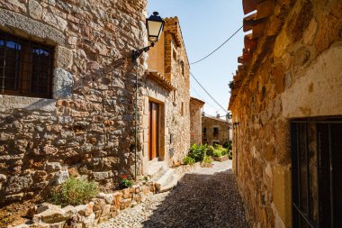 Tossa de Mar 'daki eski kasaba caddesinde. Öğlen dar bir sokakta. Taş duvarlar ve kaldırımlar. Bulutsuz gökyüzü ve keskin gölgeler. İspanya. yaz