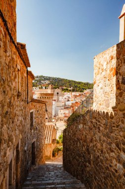 Tossa de Mar 'daki eski kasaba caddesinde. Öğlen dar bir sokakta. Taş duvarlar ve kaldırımlar. Bulutsuz gökyüzü ve keskin gölgeler. İspanya. yaz