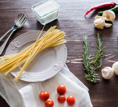 Tahta masadaki makarna malzemeleri. Tabak, çatal bıçak, makarna ve taze sebzeler.
