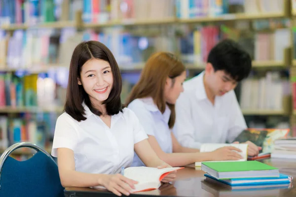 Estudante asiático senhora sorriso e ler um livro na biblioteca em universit — Fotografia de Stock