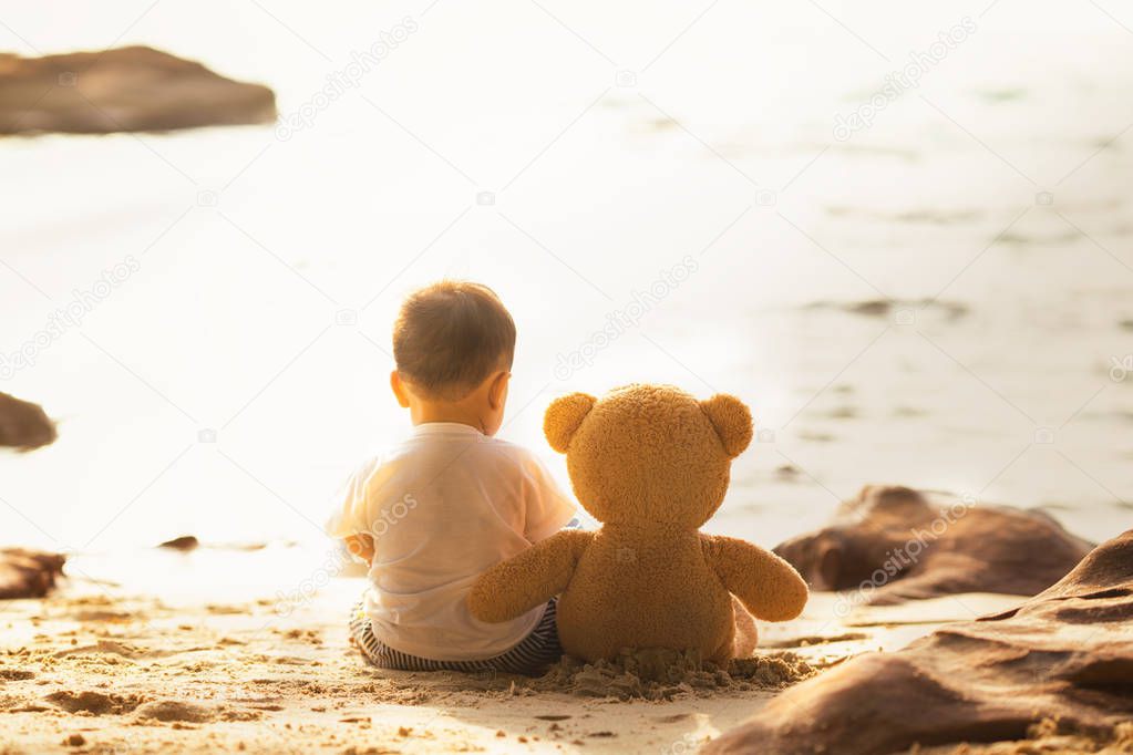 Baby and teddy bear sit togather on the beach