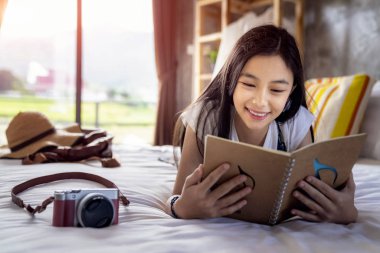 Asian girl read a travel note book on the bed in hone stay clipart