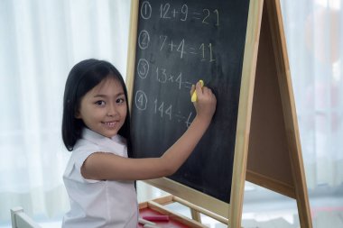 Asyalı kız arkasını dönmeden önce tahtaya yazı yazıp ödevlerini yapıyor.