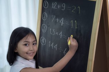 Asyalı kız arkasını dönmeden önce tahtaya yazı yazıp ödevlerini yapıyor.