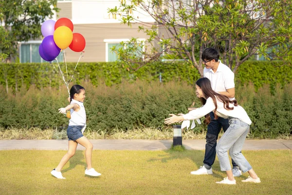 Asian daughter run with balloon on hand to her mother and her fa — 图库照片