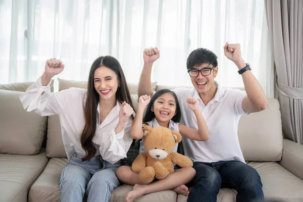 Asian fmily watching TV together on sofa in living room