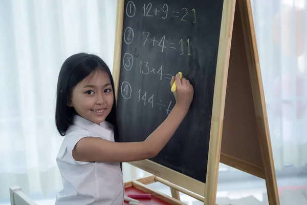 Asyalı kız arkasını dönmeden önce tahtaya yazı yazıp ödevlerini yapıyor. — Stok fotoğraf