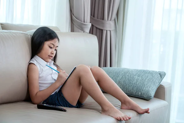 Asiatisk tjej gör hemarbete på soffan — Stockfoto