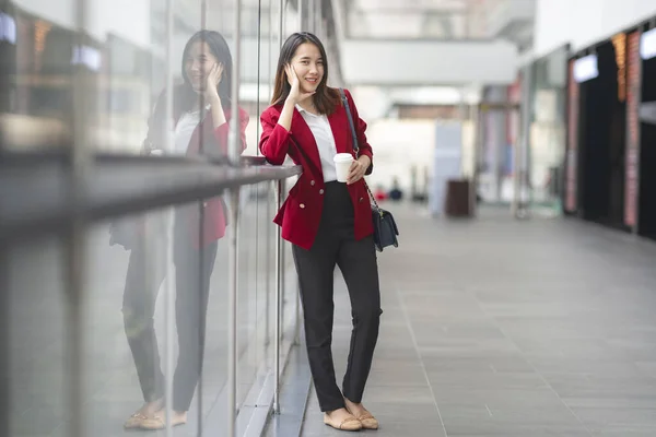 young office worker girl holding hot espresso paper cup leisurely walking on glass wall background thinking about work planning relax during lunch break time.