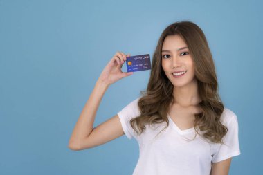 Beyaz tişörtlü güzel bir Asyalı kızın portresi kredi kartı gösteriyor ve mavi arkaplanda izole edilmiş fotokopi odasına bakıyor.