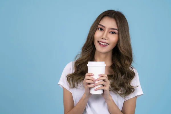 身穿白色T恤的亚洲年轻女子面带微笑 孤零零地站在蓝色的背景下 手里拿着外卖咖啡杯 — 图库照片