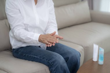 Asya 'daki yaşlılar oturma odasında kovid19 virüsünü önlemek için ellerini temizleyen alkol jeli ve nemlendirici kullanıyor..