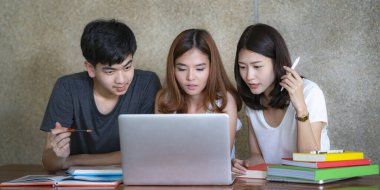 Asyalı genç erkek ve kadın karşılıklı oturup ders çalışıyor. Arkadaşlarıyla birlikte ders kitapları okuyor. Genç öğrenci kampüsü, arkadaşının arayı kapatmasına ve öğrenmesine yardımcı oluyor. Eğitim öğrenen insanlar