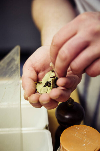 Man holds in a hand bay leaf and black pepper