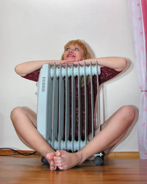 Smiling woman sitting on the floor near oil heater — Stock Photo, Image