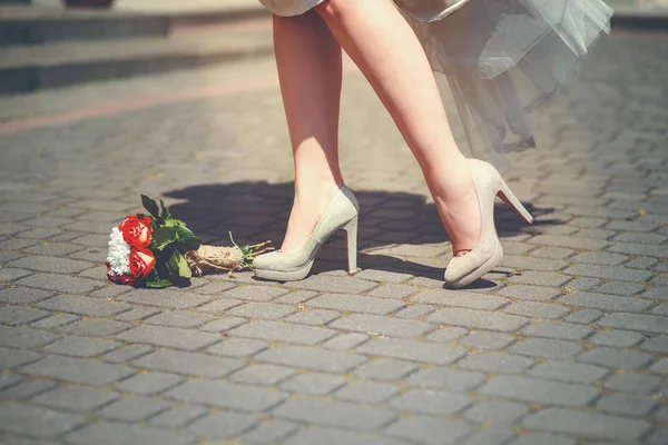 Женские ноги в блестящих туфлях на высоком каблуке возле букета с розами — стоковое фото